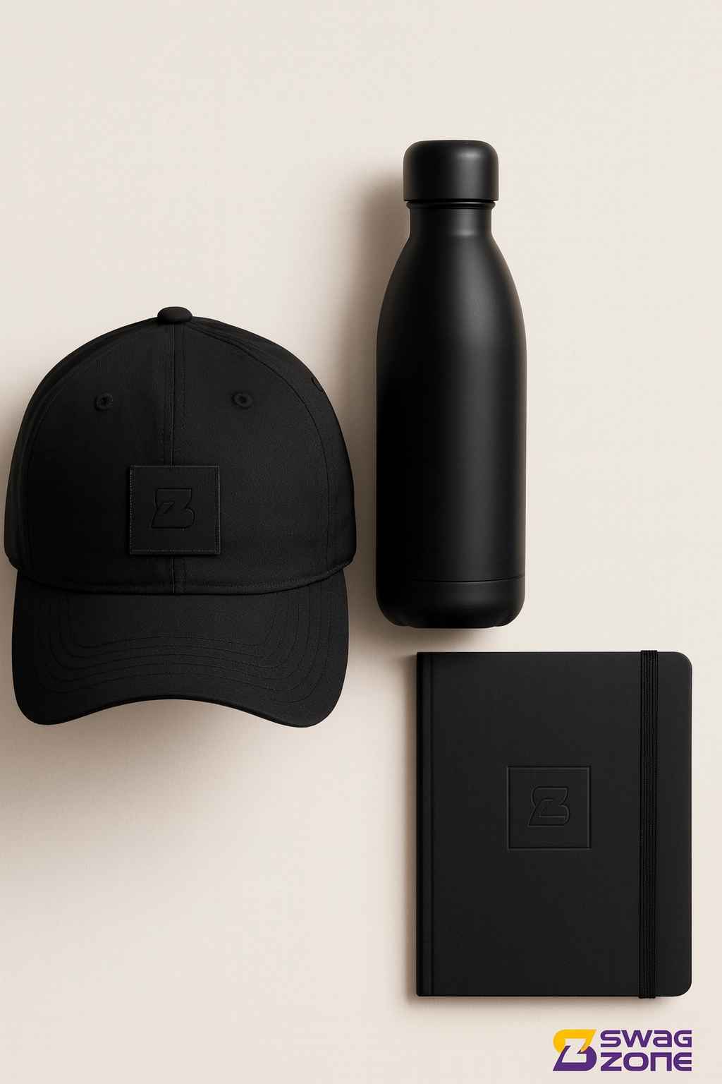 A flat lay of minimalist swag that leaves a mark, featuring a black cap, matte stainless steel bottle, and notebook with subtle SwagZone branding on a neutral background.